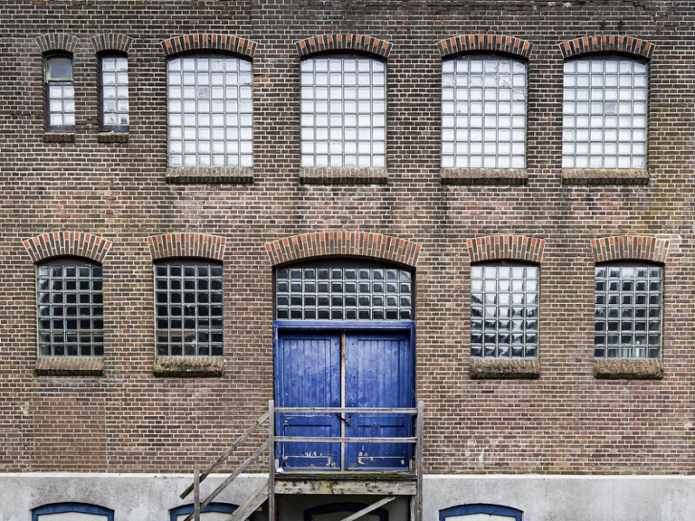 Sfeerbeeld (Unsplash): bakstenen bedrijfsgevel met glasbouwstenen en blauwe poort