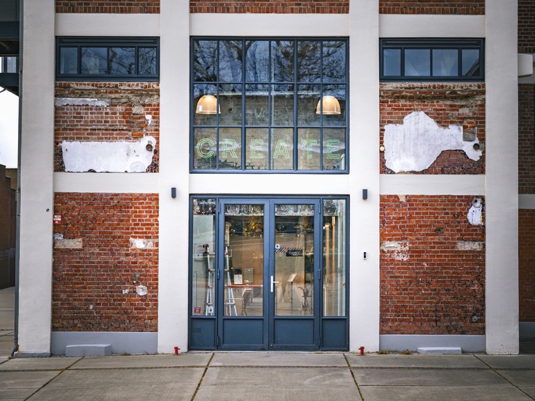 Sfeerbeeld (Unsplash): inkom van een verbouwd bakstenen gebouw met grote ramen